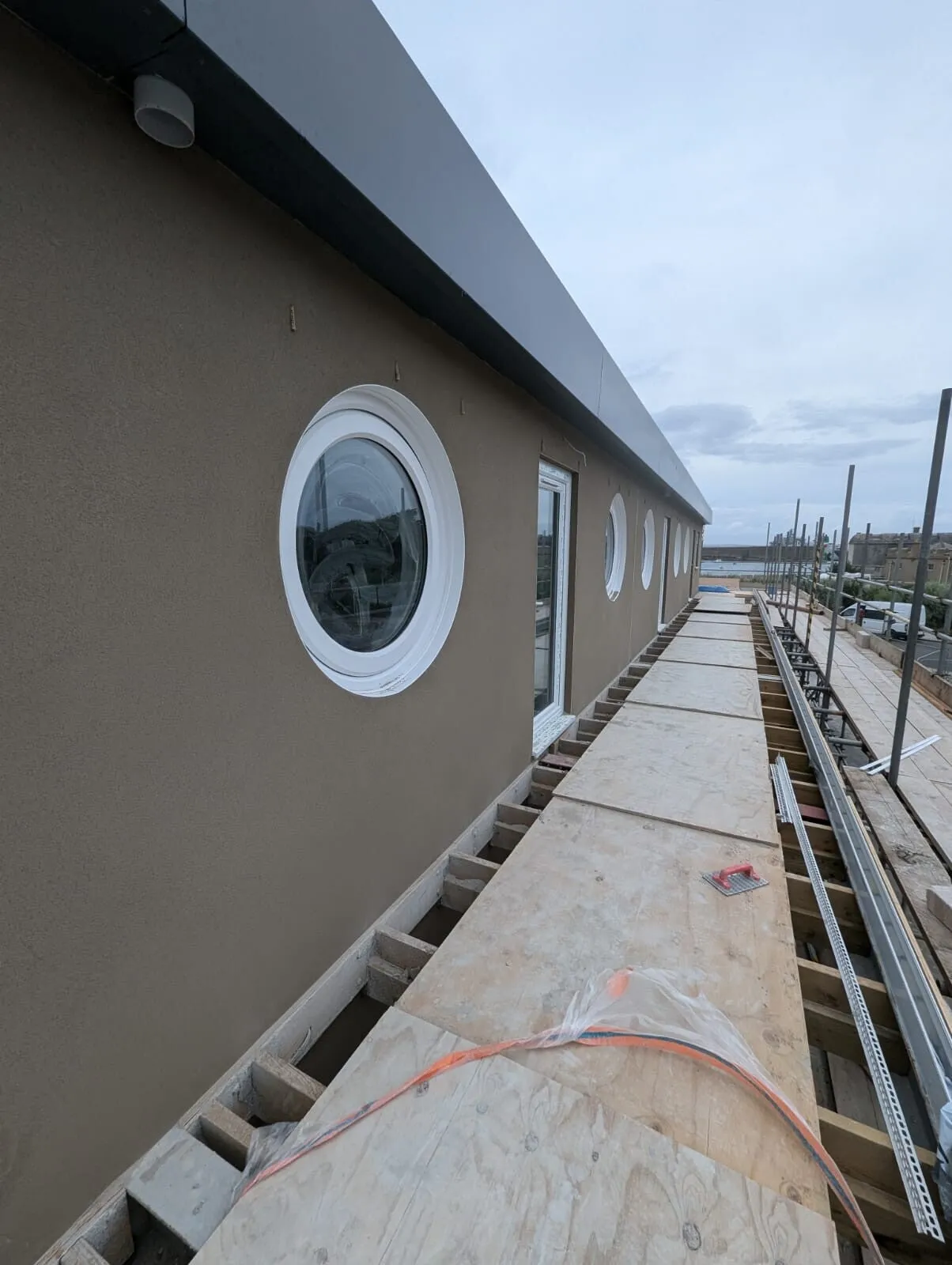 A long rendered wall with porthole windows, seen from the scaffold