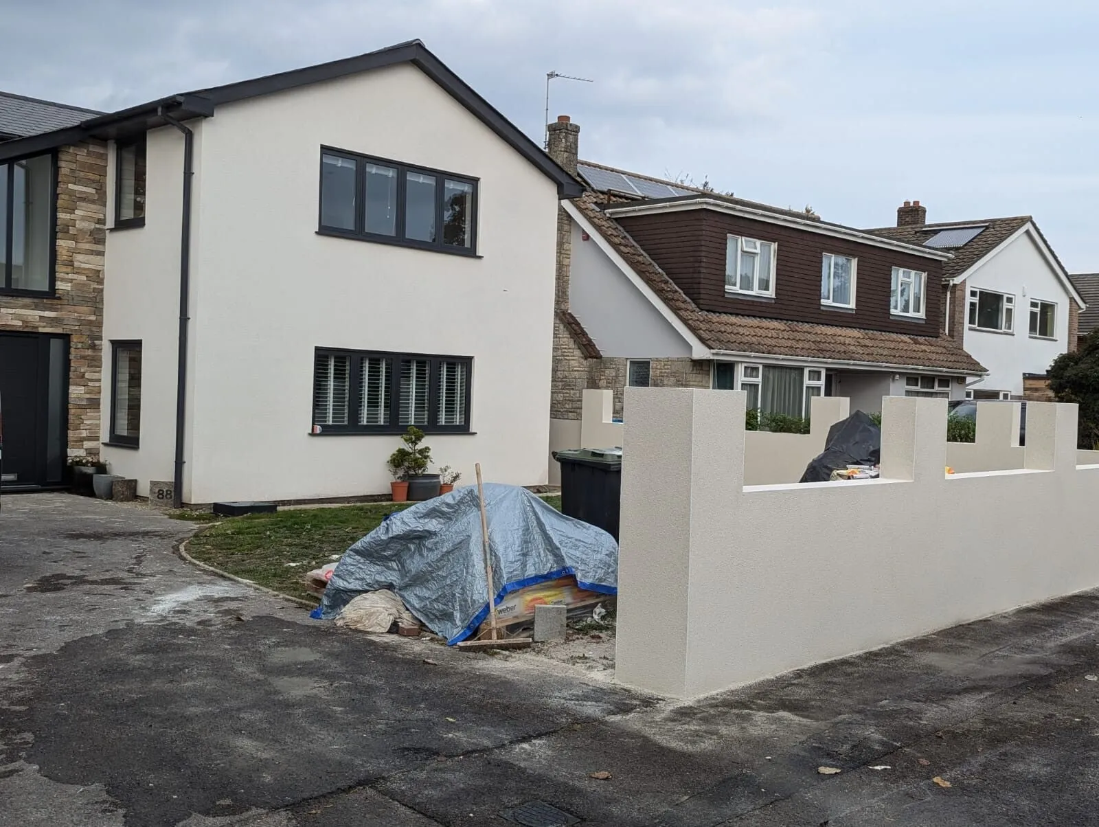 A two-storey house and a new garden wall, both rendered in cream