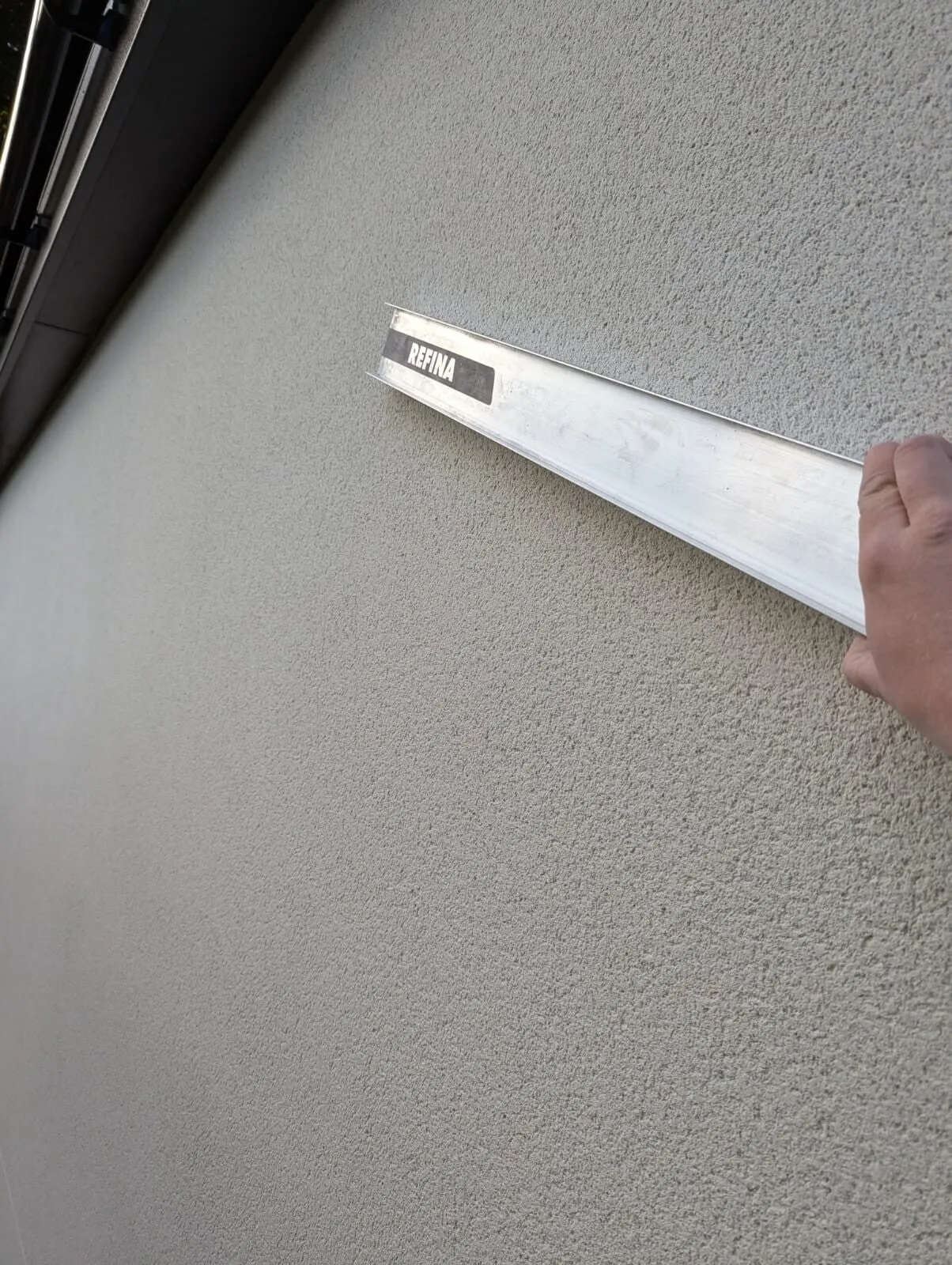Close up of Adept’s textured spray render finish, a Refina straightedge laid across it