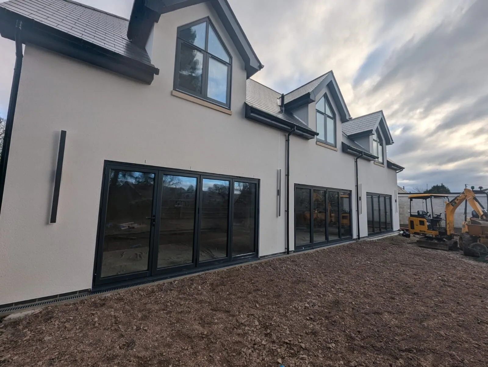 The side of a new build in cream render, with bifold doors
